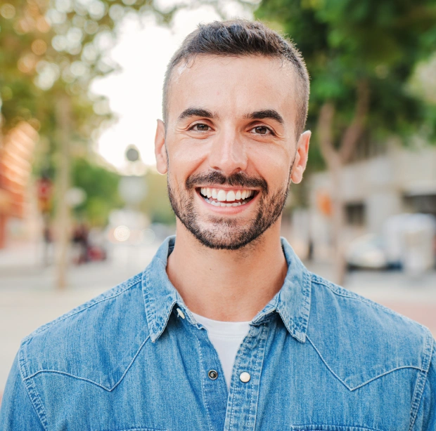 Portrait of a smiling man in a denim shirt in an outdoor setting