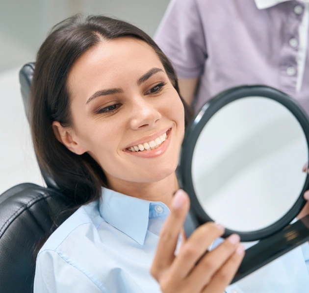 Woman smiling and holding a small mirror during a dental appointment