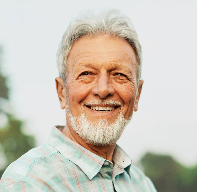Older man with white hair and beard smiling warmly outdoors