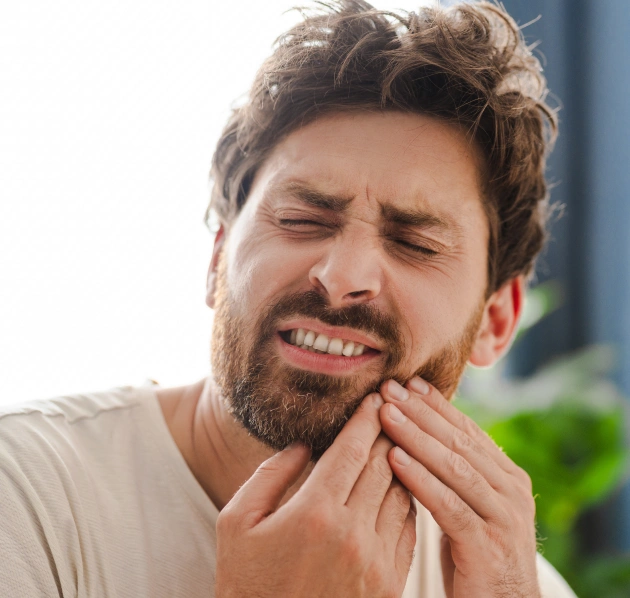 Middle aged man grimacing and holding his jaw in pain