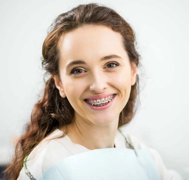 Mujer joven con aparatos dentales sonriendo con confianza sobre un fondo claro.