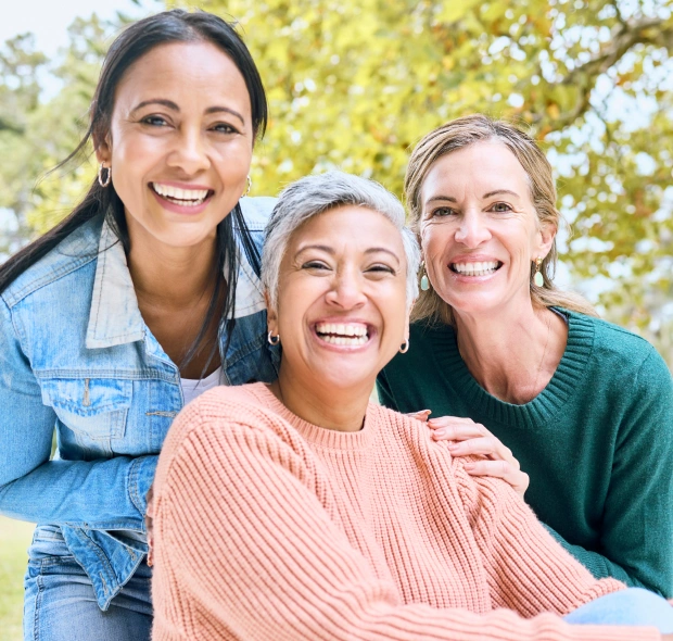 Three women smiling and posing together outdoors in casual clothing