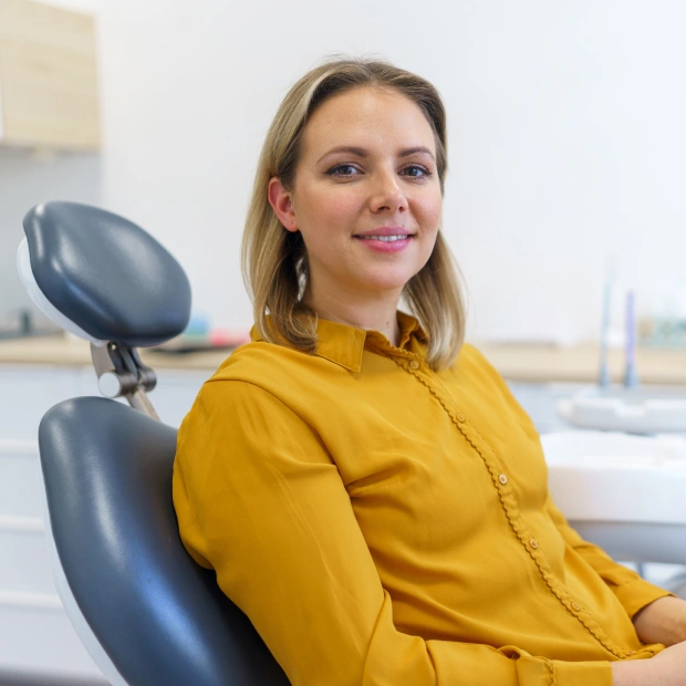 Female patient in a yellow top smiling while seated in a dental chair