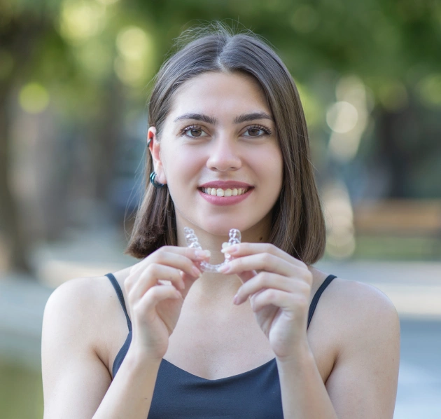 Young woman holding a clear aligner tray and smiling