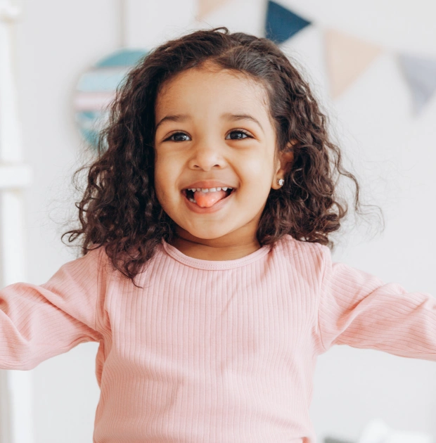 Young girl in a pink top smiling at the camera against a light background