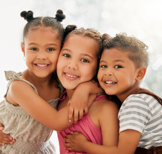 Three young girls hugging and smiling at the camera outdoors