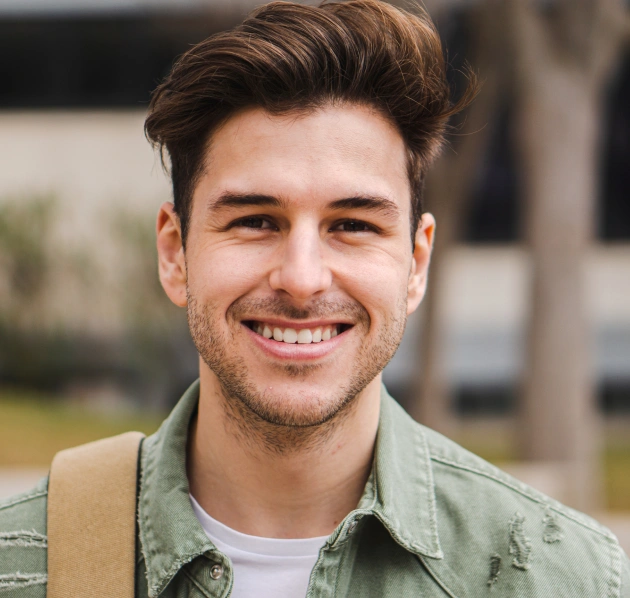 Retrato de un joven sonriente con cabello corto y oscuro sobre un fondo neutro.