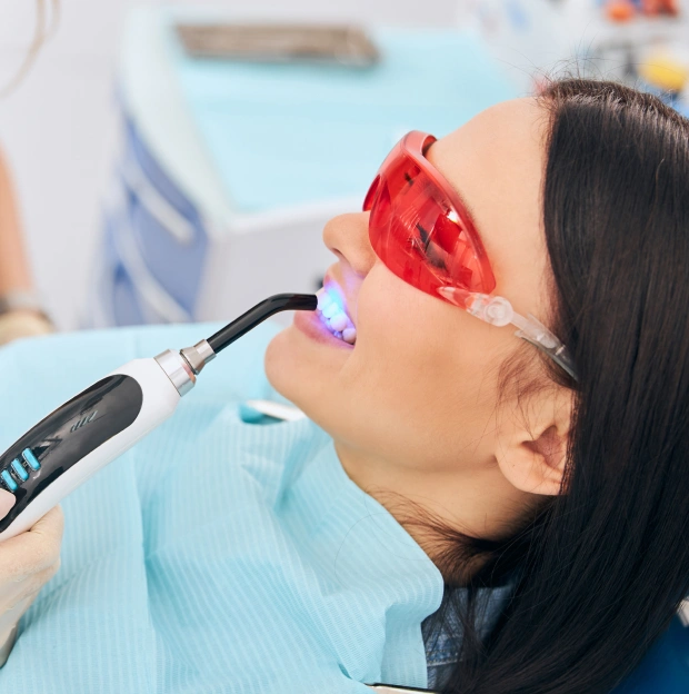 Dentist using a whitening device on a female patient wearing protective glasses