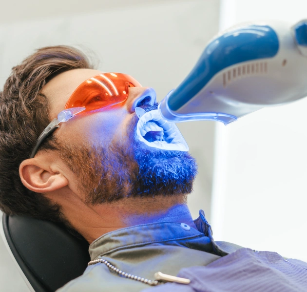 Dentist applying a whitening treatment using a UV curing light on a patient