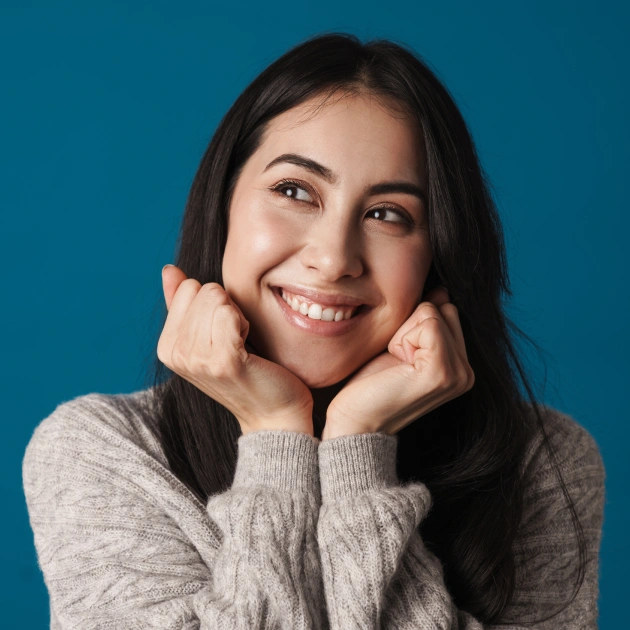 Portrait of a young woman with dark hair smiling and resting her chin on her hands