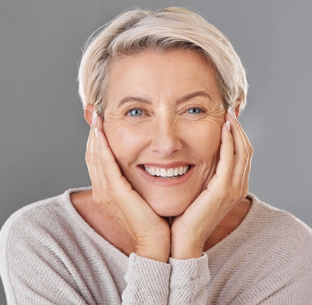 Older woman with short white hair smiling and resting her hands on her cheeks