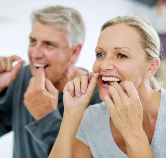 Couple smiling and flossing their teeth together at home