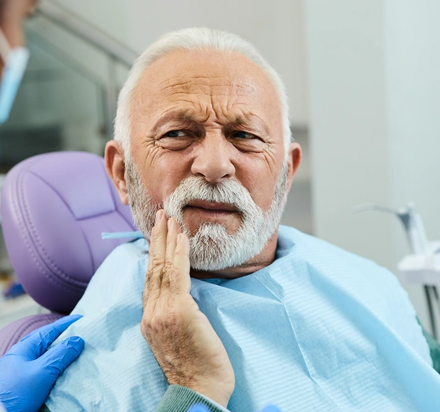 Elderly man in a dental bib holding his jaw during a dental appointment