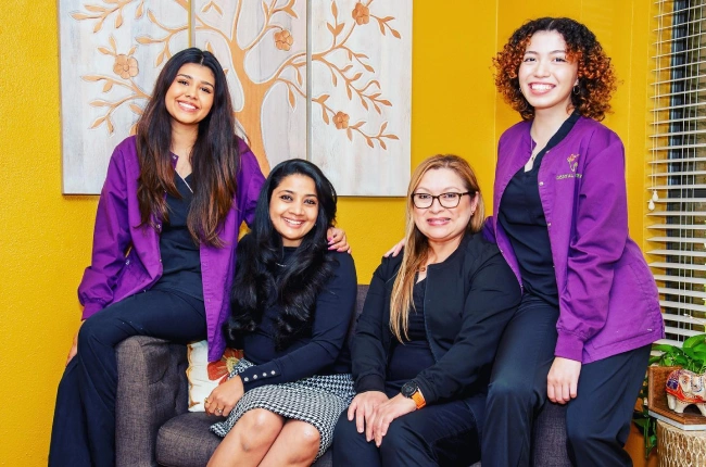 Dental Artistry Irving team of four smiling female staff members seated together in the office