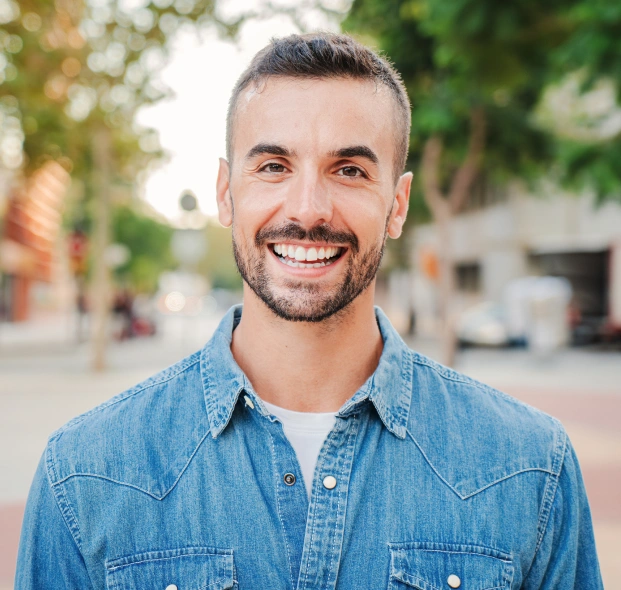 Portrait of a smiling man in a denim shirt against a neutral background