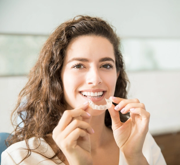 Young woman holding a clear aligner tray close to her face and smiling