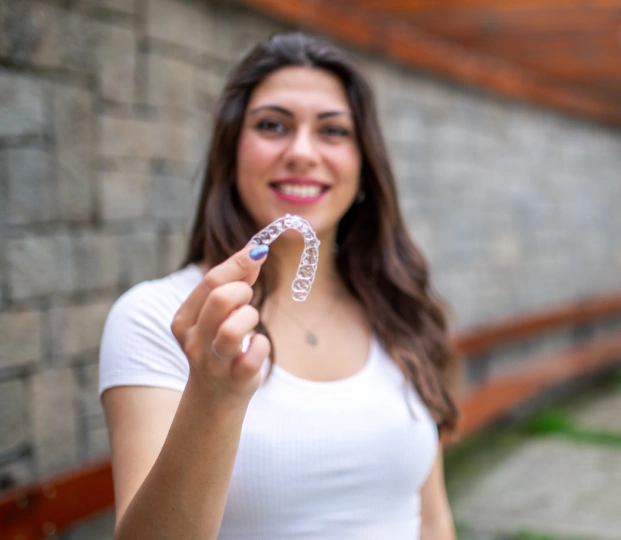 Young woman holding a clear aligner and smiling in a casual setting