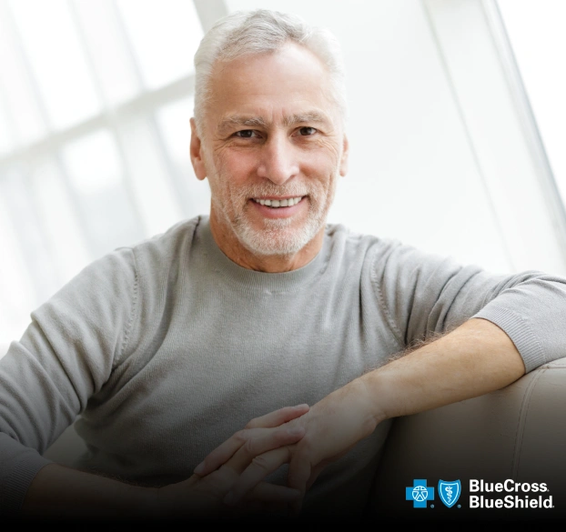 Portrait of a smiling older man in a casual grey top with a Blue Cross Blue Shield logo overlay