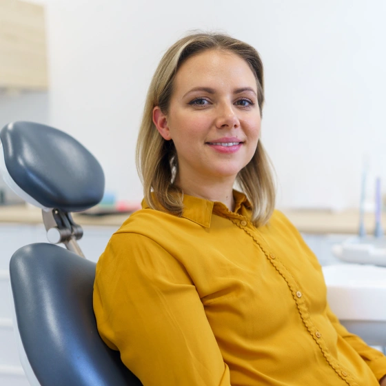 Female patient in a yellow top smiling while seated in a dental chair