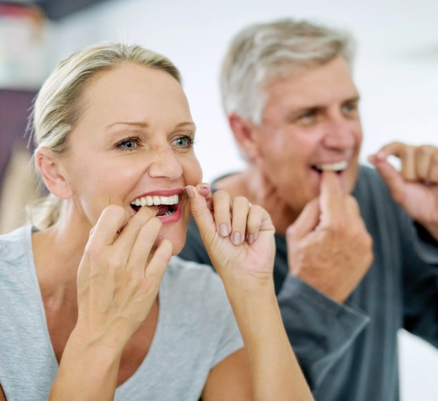 Older couple smiling and flossing together during a demonstration