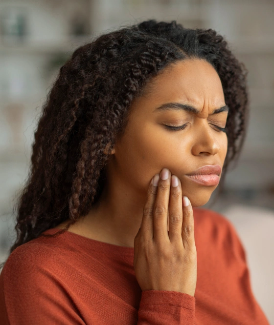 Young woman holding her cheek in pain against a dark background