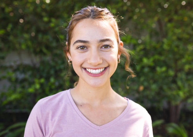 Portrait of a smiling young woman in a lavender top against a light background