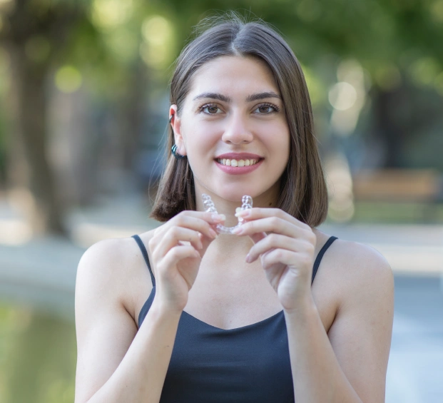 Young woman holding a clear aligner and smiling in a casual setting
