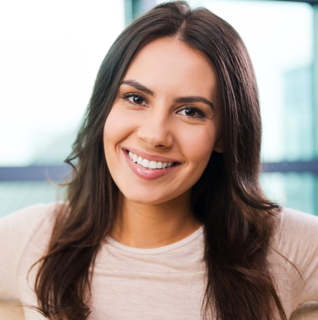 Portrait of a young woman with dark hair smiling against a light background