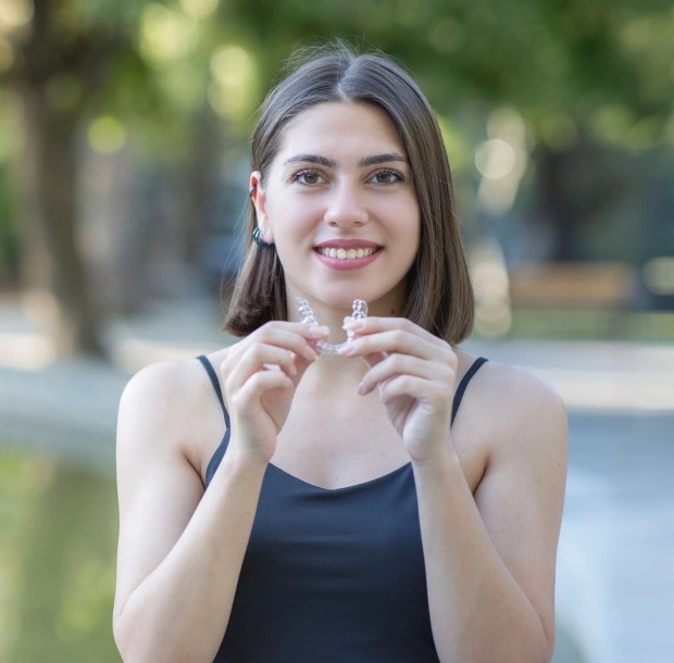Young woman holding a clear aligner and smiling in a casual setting