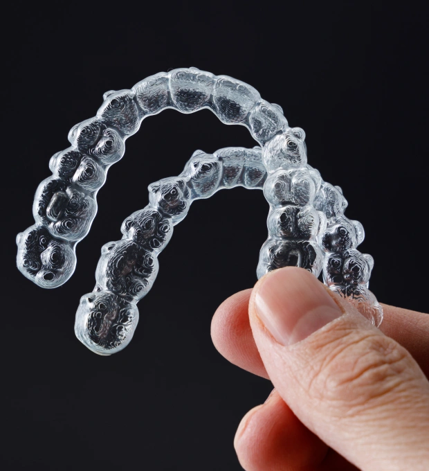 Hand holding a clear Invisalign aligner tray against a dark background