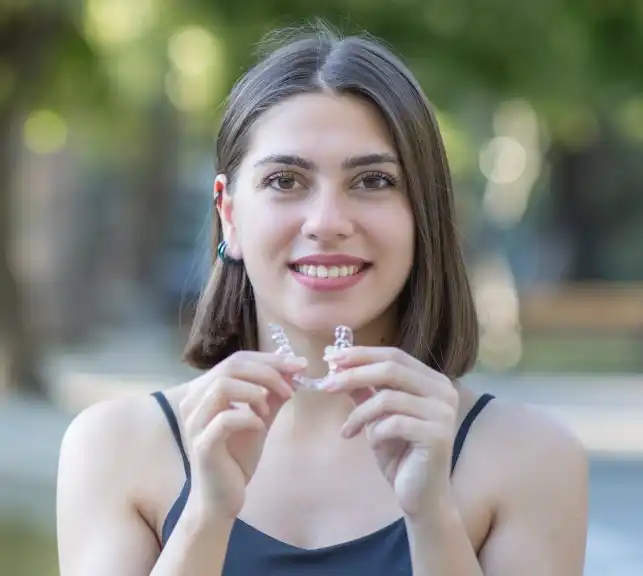 Young woman holding a clear aligner and smiling in a casual setting