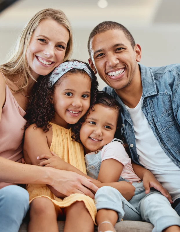 Smiling family of four, with parents and two young children posing closely together.