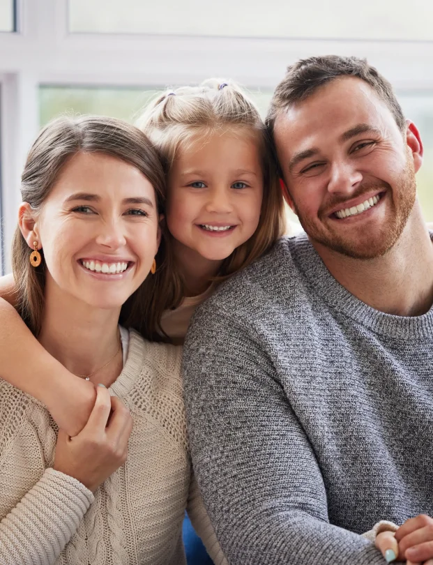 Smiling family of three, with a mother, young daughter, and father posing together.
