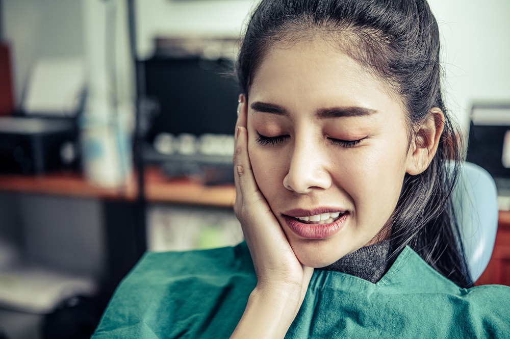 a girl seating on dentist chair and having tooth pain and she needs emergency dental treatment in Houston