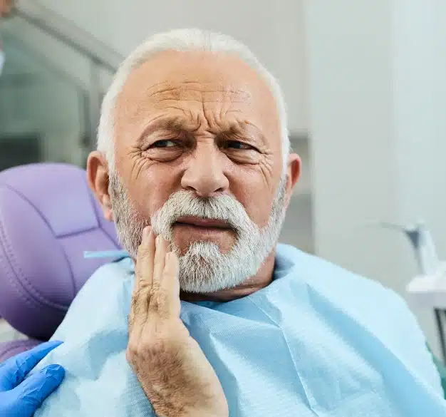 Older male patient holding his jaw in pain before tooth extraction treatment at The Dentist Place of Clearwater in Clearwater, FL