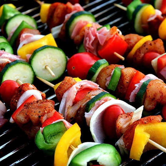 Colorful vegetable and meat skewers grilling on barbecue grates with peppers, onions, and zucchini.