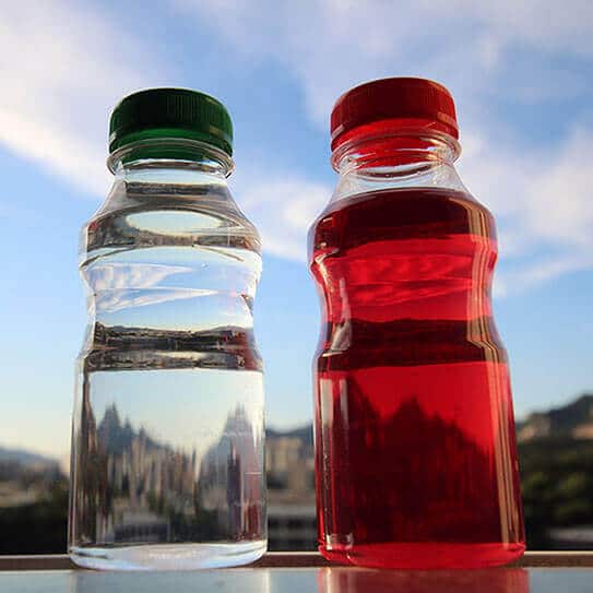 Two beverage bottles with green and red caps against blue sky and mountain backdrop.