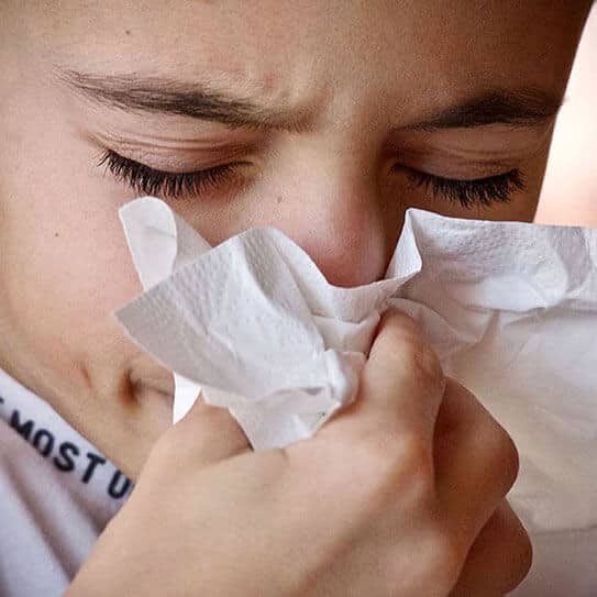 Child blowing nose into tissue, appearing sick or unwell.