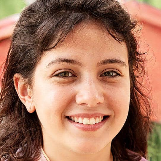 Young woman smiling brightly outdoors, showcasing healthy teeth and a warm expression.