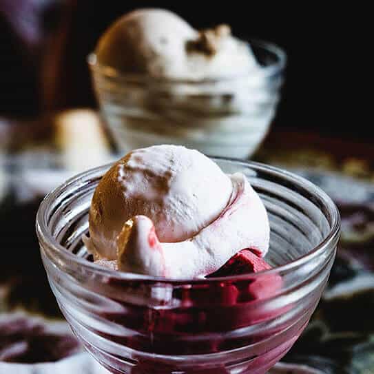 Scoops of ice cream in glass bowls with dark syrup, dessert presentation on dark surface.
