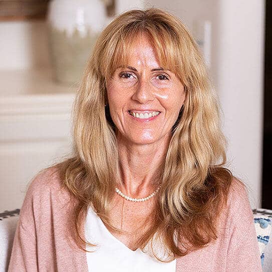 Professional woman smiling at camera in dental office setting, wearing pink cardigan.