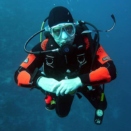 Scuba diver in orange and black gear underwater with blue ocean background
