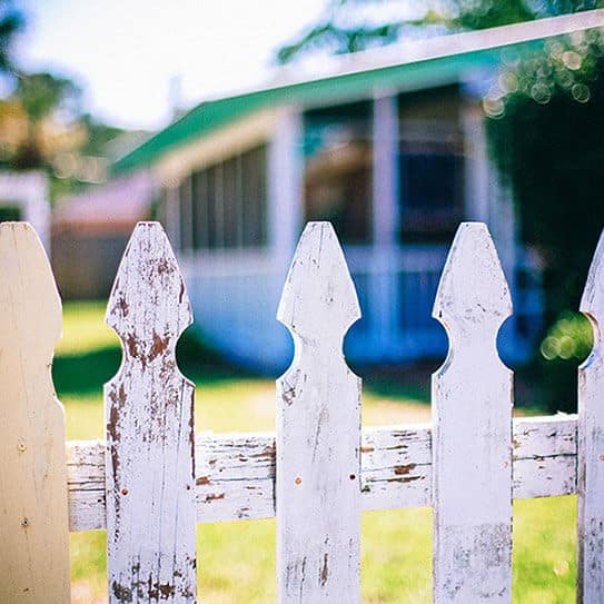 White picket fence with suburban house and green lawn in background