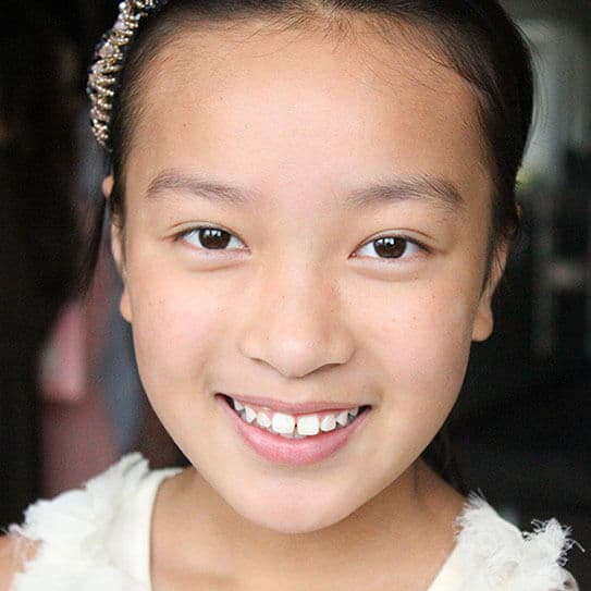 Young girl smiling at camera, showcasing healthy teeth in professional headshot.