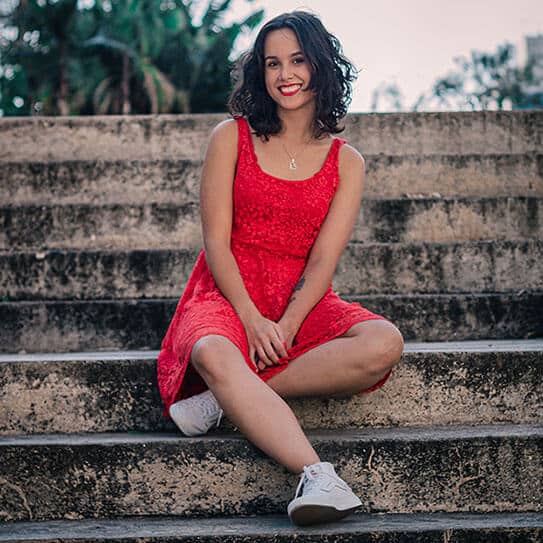 Young woman in red dress sitting on stone steps outdoors.