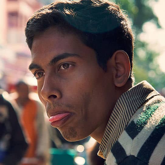 Man with thoughtful expression outdoors in casual striped sweater, blurred background.