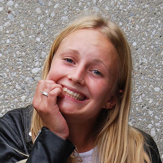 Young girl smiling brightly with hand near face against textured gray background.