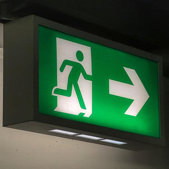 Green emergency exit sign with running figure and rightward arrow on wall.