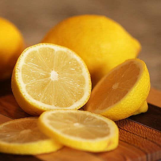 Fresh cut lemons on wooden surface, whole lemons blurred in background.