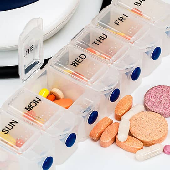 Weekly pill organizer displaying medications labeled by day, with various tablets and capsules arranged in compartments.